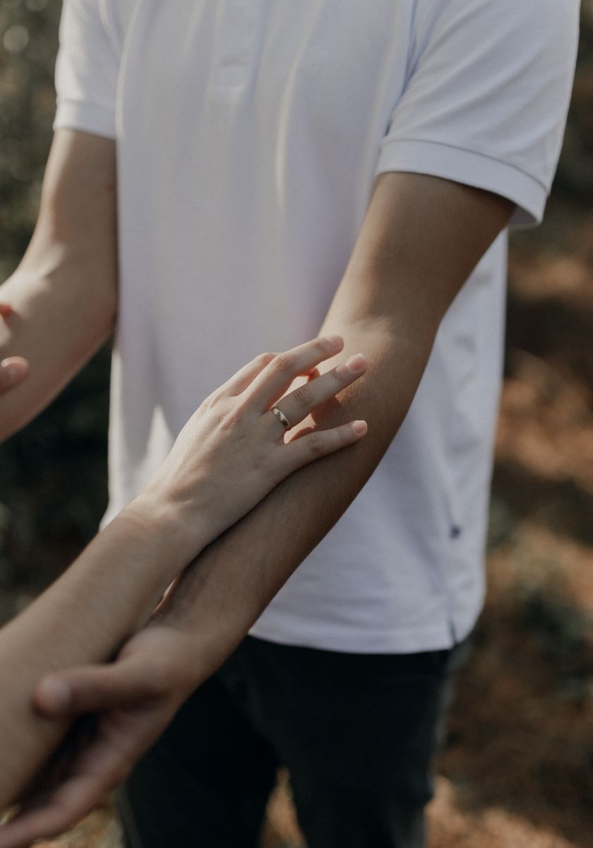 A close-up of a couple touching hands outdoors, symbolizing connection and affection.