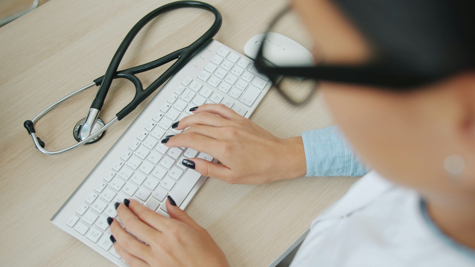 A clinician typing at a keyboard with a stethoscope resting on the desk