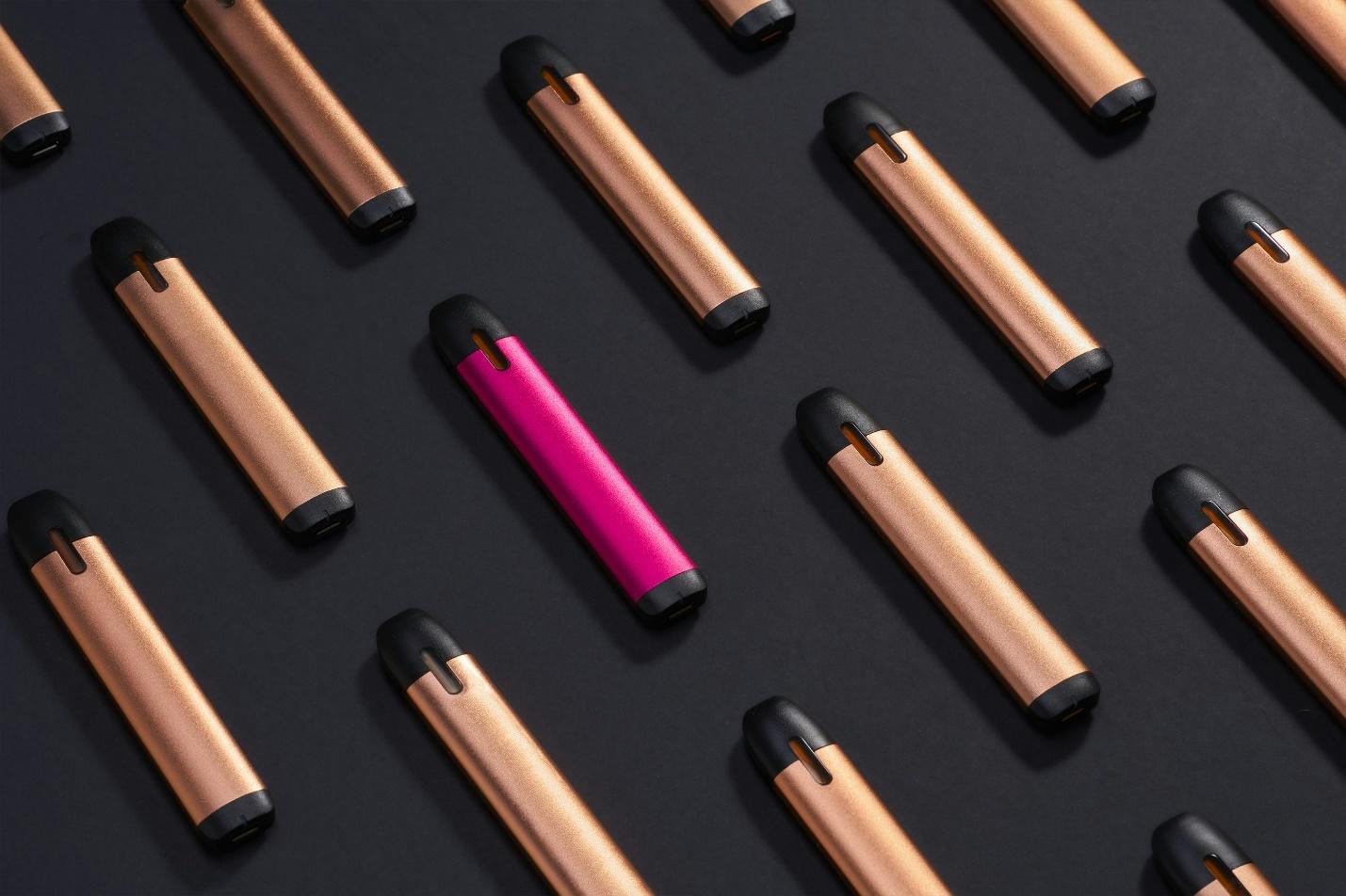 Lineup of THC vape pens in gold and pink on a dark background