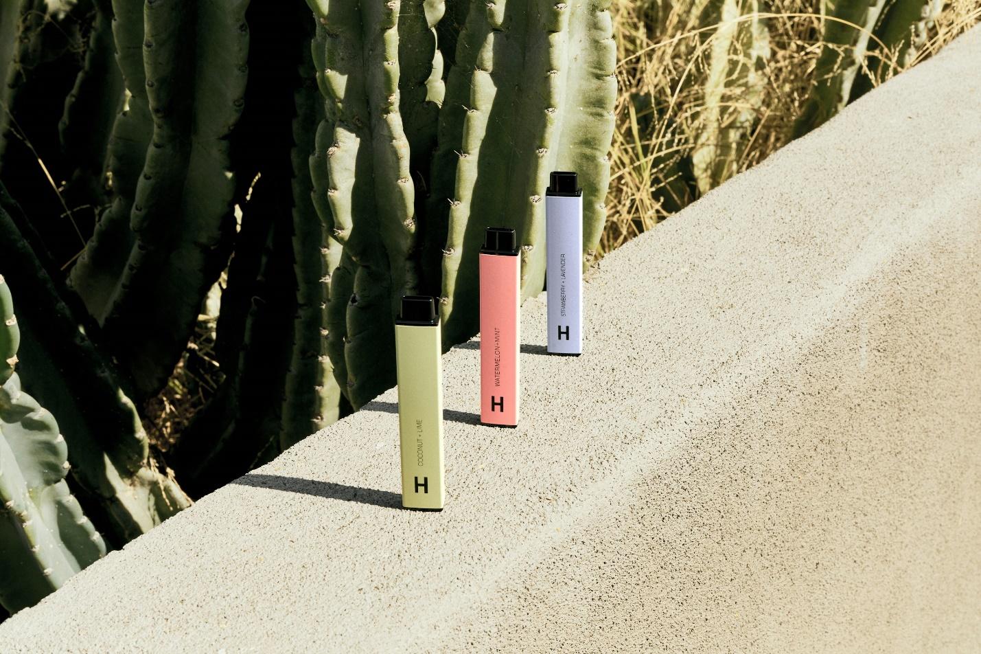 Three disposable THC vape pens in pastel colors on a stone ledge