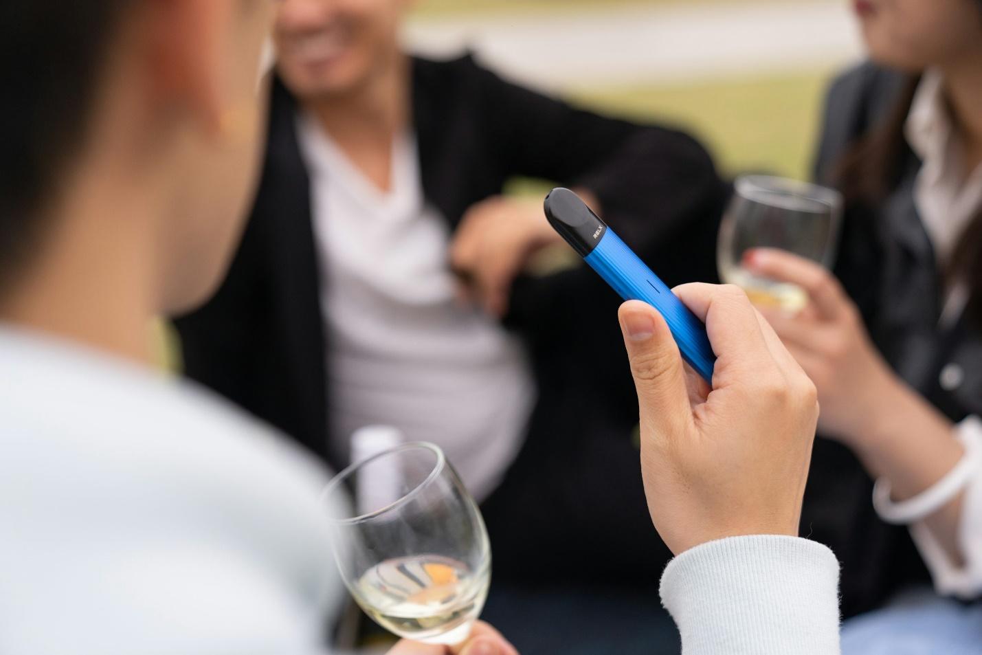 Hand holding a blue THC vape pen at an outdoor gathering