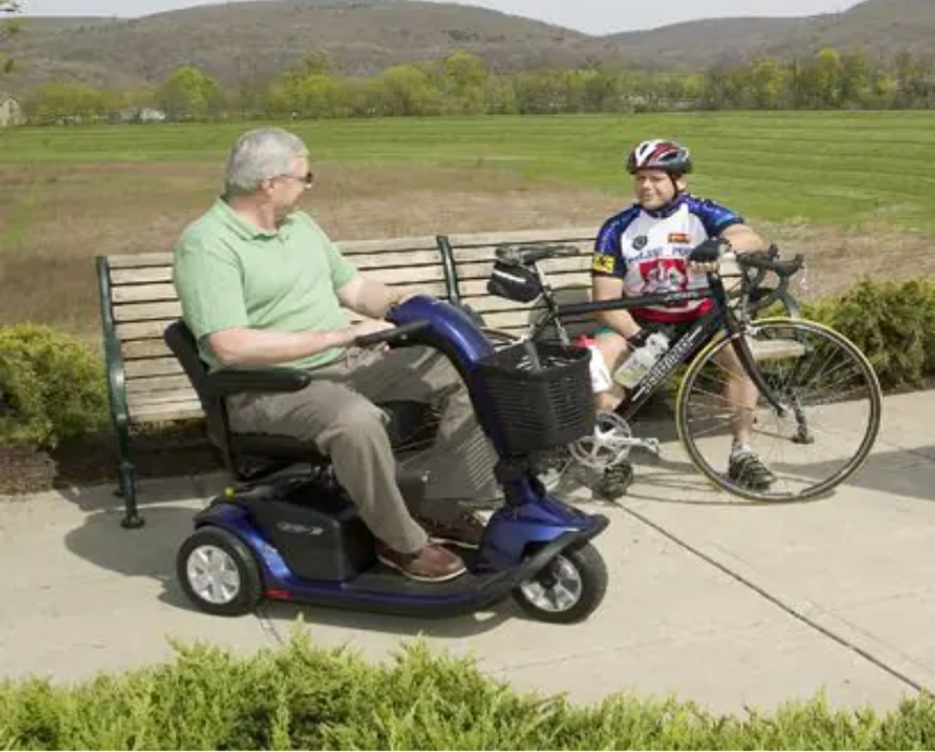 Man riding a blue Pride mobility scooter outdoors on a paved path
