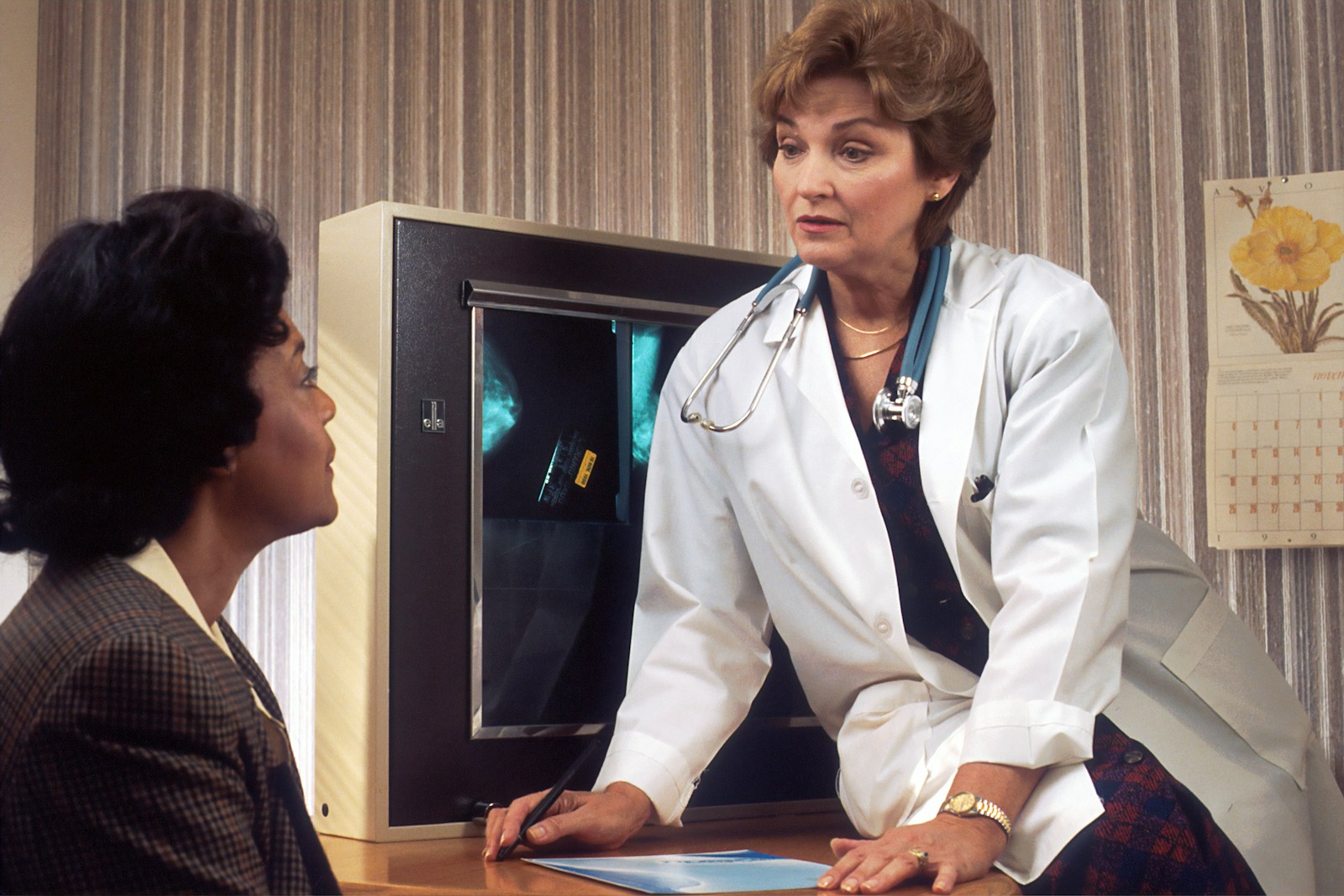 Doctor sitting on desk talking to sitting woman