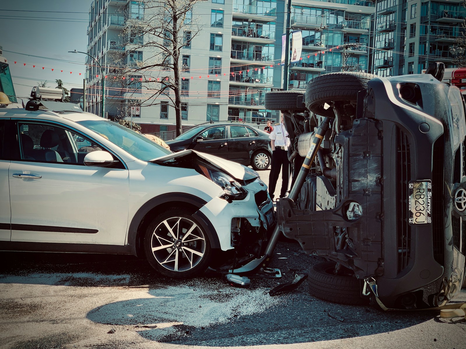 Overturned black car on a city street after a collision, with a damaged silver car nearby