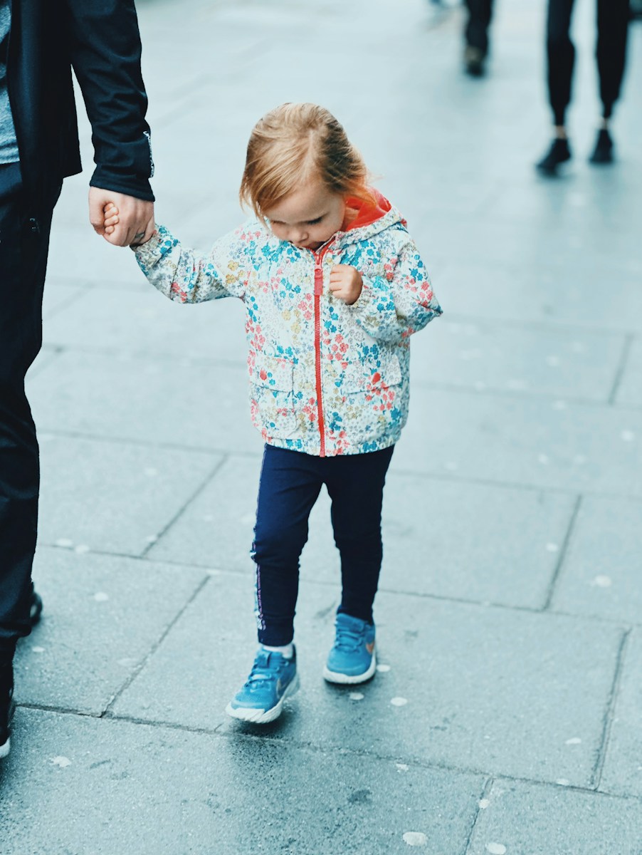 A young girl holds a hand while walking on pavement